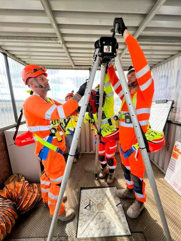 Workers working with harness safety and rescue equipment at a tripod